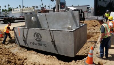 A Newterra Clara filter is lowered into a prepared dirt site at an auto recycler with four technicians guiding the unit or looking on as a crane lowers the concrete box and divider into place