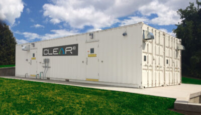 ANewterra Clear3 decentralized membrane bioreactor consisting of a white shipping container with locking doors and branded with the Clear3 logo on a concrete slab in an outdoor setting with green grass and blue skies