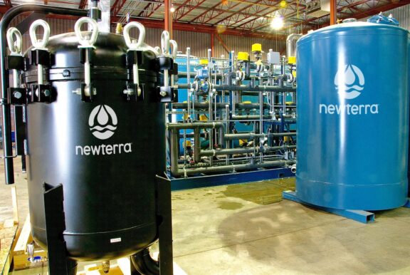 Two Newterra branded elevated tank vessels connect to a ground remediation system in an industrial processing buiding