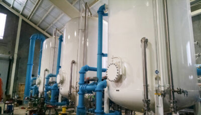 Three white Cansorb high pressure liquid phase active carbon adsorbers installed in an industrial warehouse with blue pipes entering and exiting each unit