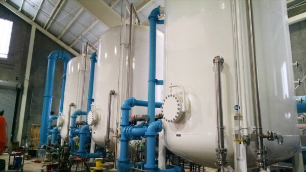 Three white Cansorb high pressure liquid phase active carbon adsorbers installed in an industrial warehouse with blue pipes entering and exiting each unit