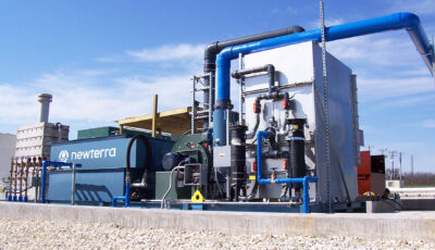 Newterra vacuum extraction system consisting of a series of metal boxes connected by pipes and hoses with the center blue box branded with the Newterra logo and the box on the right connected to a blower motor, pipes of various sizes with gauges and electrical panels in an industrial setting, the unit rests on a concrete slab near power lines