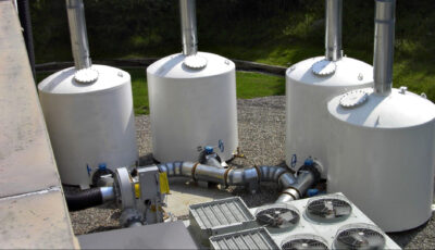 Four Newterra filters sit outside an industrial site with large pipes entering each filter vessel with a valve wheel