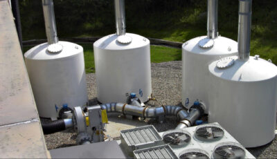 Four Newterra filters sit outside an industrial site with large pipes entering each filter vessel with a valve wheel