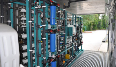 Interior view of a Seamega modular water desalination system consisiting of a cyan metal frame, various horizontally positioned filtration pipes, horizontal filters, electrical panels, and various pipes connecting the equipment to a water tank all located inside of a shipping container