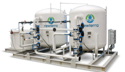 A product image with a white background of a Cochrane by Newterra water softening system consisting of a water tank connected to two elevated white vessels branded with Newterra logos, the entire system is supported by a metal frame and connected throughout with metal pipes with filters and components installed on the pipes, an electrical panel accompanies the unit