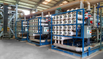 Three reverse osmosis Delta units installed on a concrete slab inside an industrial warehouse with each unit consisting of horizontally oriented plastic filtration pipe units stacked within a blue metal frame along with an electrical panel and pipes of various sizes with valve and gauge components