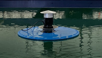 Above surface view of the Newterra Halo surface splasher aerator made of a blue metal disc with a lip and metal and black finish components terminating to a shallow metal cone as the unit aerates waste water in an indoor treatment pond