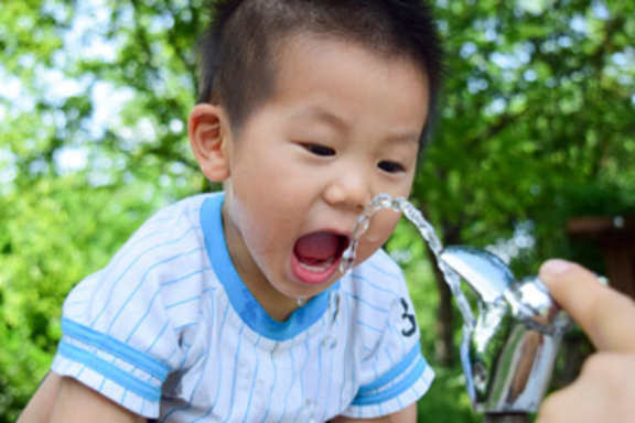 An child of Asian descent drinks water from a public drinking fountain