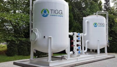 Two Cansorb high pressure liquid phase active carbon adsorbers connected by pipes filter water in a designed environment, system mounted on concrete slabs with cars in a parking lot nearby