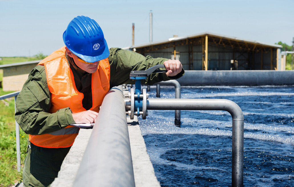 A wastewater engineer controls the quality of water and aerated activated sludge tank at a waste water treatment plant by turning a compound valve in accordance to figures on a clipboard
