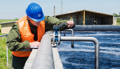 A wastewater engineer controls the quality of water and aerated activated sludge tank at a waste water treatment plant by turning a compound valve in accordance to figures on a clipboard