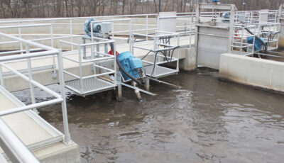 A concrete open containment pond with service walkways and metal platforms support the Newterra Triton 2.0 process aerator mixer with a bridge mount; water moves as the unit mixes the treatment water