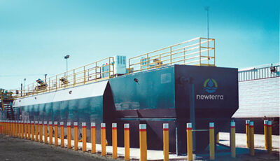 Newterra's Unisystem water treatment plant technology consisting of a large blue painted box and tank with walking railing on top and surrounded by drive proof yellow posts