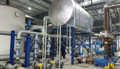 An elevated tank supported by blue steel i-beams stands above various pipes in front of the tank that connect to additional input pipes for wastewater to flow into the tank for treatment
