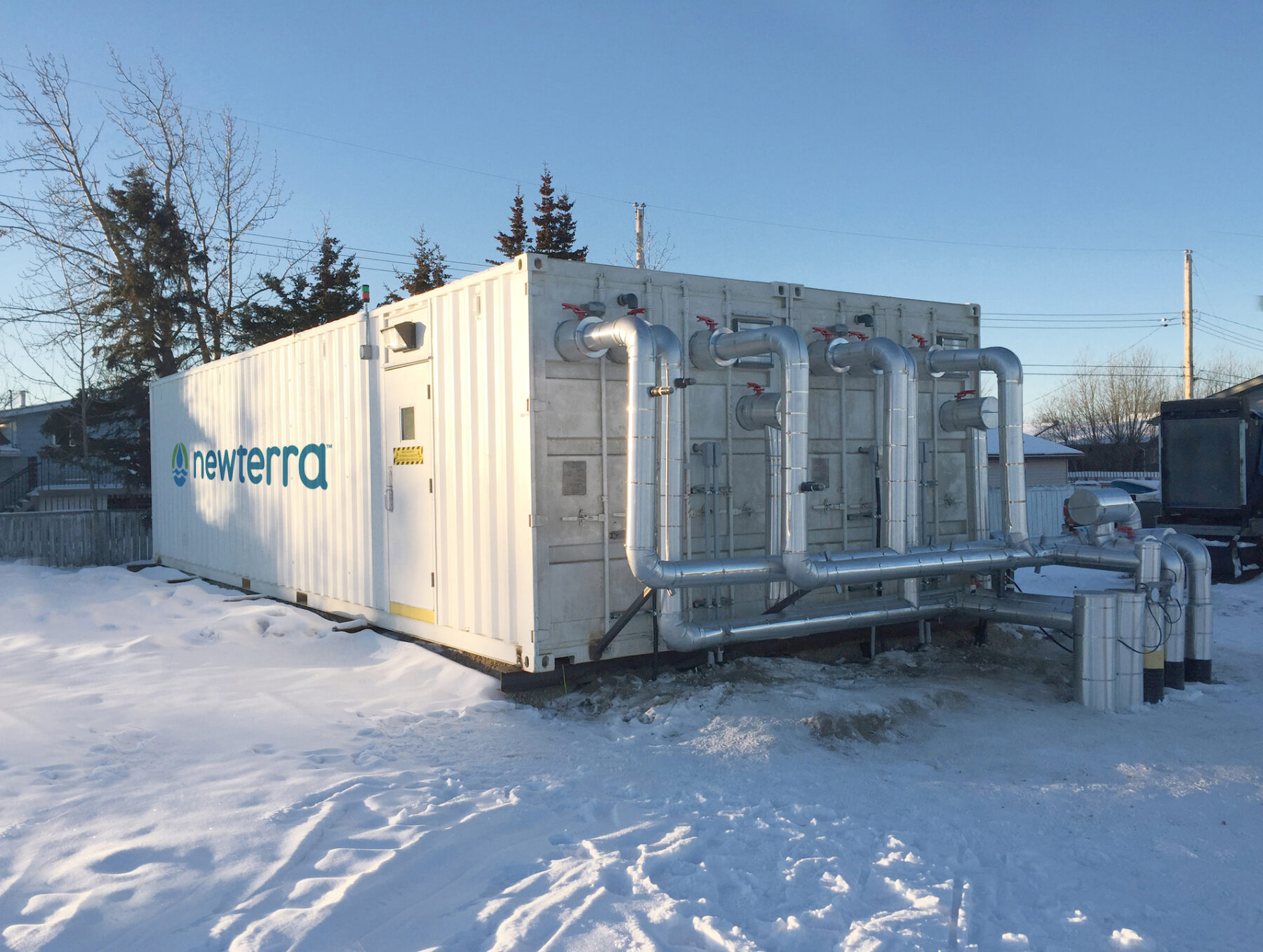 Newerra modular wastewater treatment technology consisting of a double wide shipping container with eight pipes connecting to a water in or outflow for treating water in a winter setting
