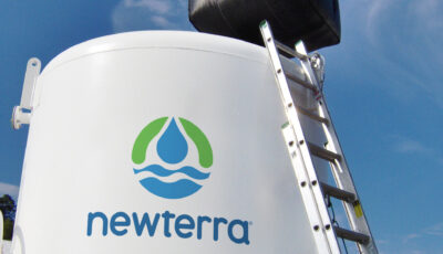 Activated carbon is added to a Newterra tank by a large forklift via an industrial fabric bag, a metal ladder rests against the white tank branded with Newterra's logo