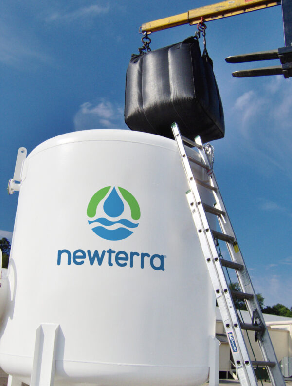 Activated carbon is added to a Newterra tank by a large forklift via an industrial fabric bag, a metal ladder rests against the white tank branded with Newterra's logo