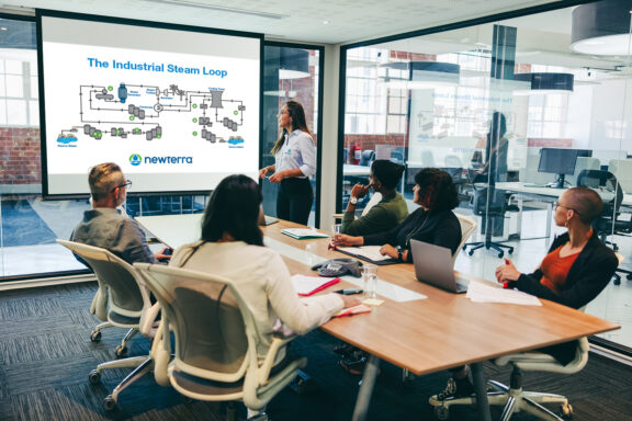 Five professionals sit around a conference table paying attention to a speaker in front of a projected diagram of The Industrial Stream, a Newterra branded presentation.