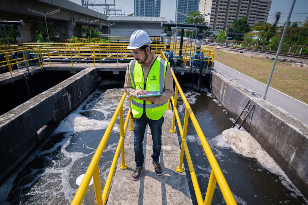 A Newterra technician takes notes on water quality on a platform protected by yellow guard rails over a concrete containment pond being treated with aeration technology.