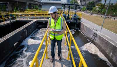 A Newterra technician takes notes on water quality on a platform protected by yellow guard rails over a concrete containment pond being treated with aeration technology.