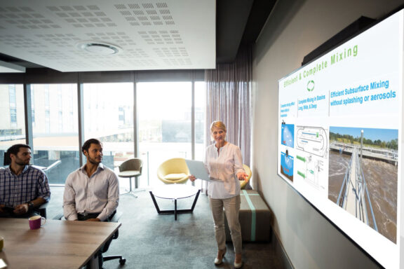 A mature woman presents a pitch of efficient and complete mixing to a group of professionals in a modern conference room