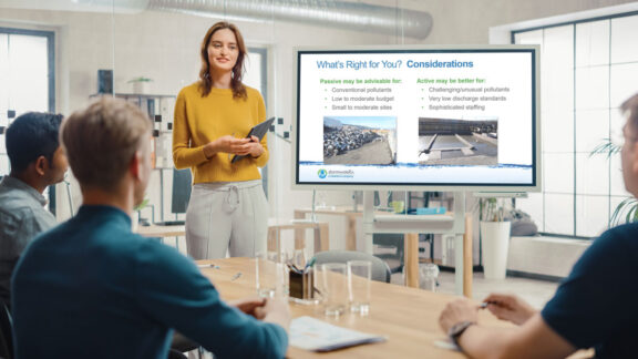 Three men watch a female speaker presenting a pitch about Newterra technologies in a professional, modern office environment