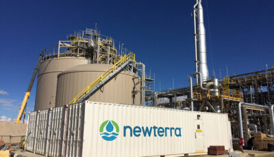 Modular water treatment technology contained within a Newterra branded shipping container with large beige storage tanks behind four modular units