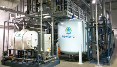 Industrial water treatment technology inside a building featuring metal and plastic tanks with pipes extending in many directions with walking platform over the tanks