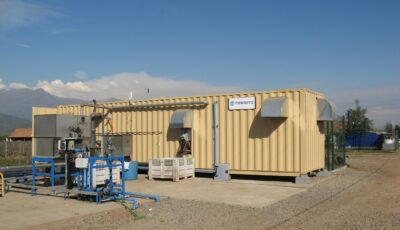 Pale yellow shipping container modular food and beverage water treatment solution sits outdoors on a concrete slab