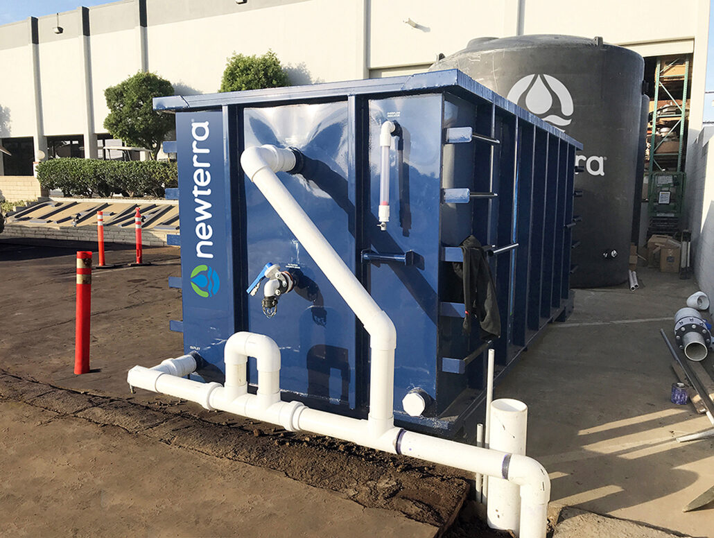 Industrial stormwater solution consisting of a shipping container with PVC plastic tubes extending in and around the unit in front of a water holding tank branded with Newterra's logo.