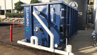 Industrial stormwater solution consisting of a shipping container with PVC plastic tubes extending in and around the unit in front of a water holding tank branded with Newterra's logo.