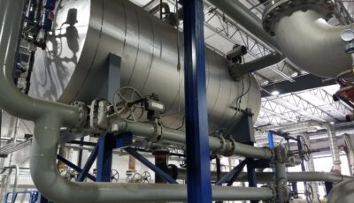 Industrial spray atomizing deaerator in an elevated installation with steel cylindrical tank near the ceiling in an industrial application surrounded by steel pipes and blue support