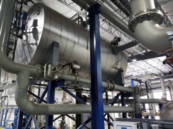 Industrial spray atomizing deaerator in an elevated installation with steel cylindrical tank near the ceiling in an industrial application surrounded by steel pipes and blue support