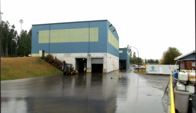 Flooding of an industrial building outdoors showing a blue and pale green building with white foundation submerged and garage stalls open, image has gradient of black to light grey on all sides top start black and fades left to right with the dark color starting the next side forming a pattern of dark to light.