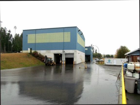 Flooding of an industrial building outdoors showing a blue and pale green building with white foundation submerged and garage stalls open, image has gradient of black to light grey on all sides top start black and fades left to right with the dark color starting the next side forming a pattern of dark to light.