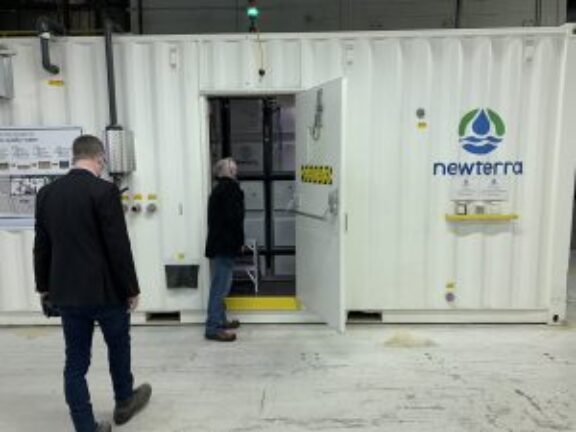 Two men inspect Newterra's toilet to tap technology housed in a white shipping container branded with Newterra's logo and brand name