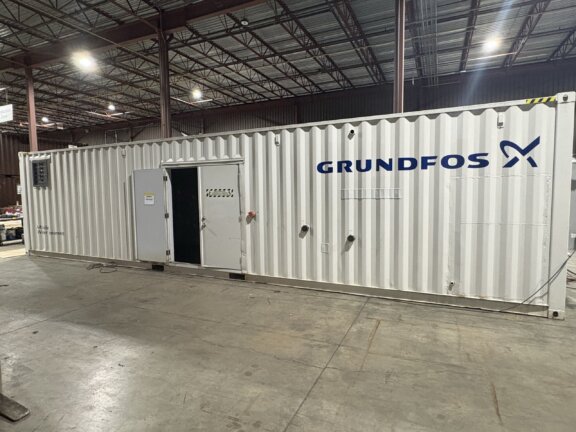 White shipping container in a large industrial warehouse with exposed steel beams and bright lights in the ceiling.