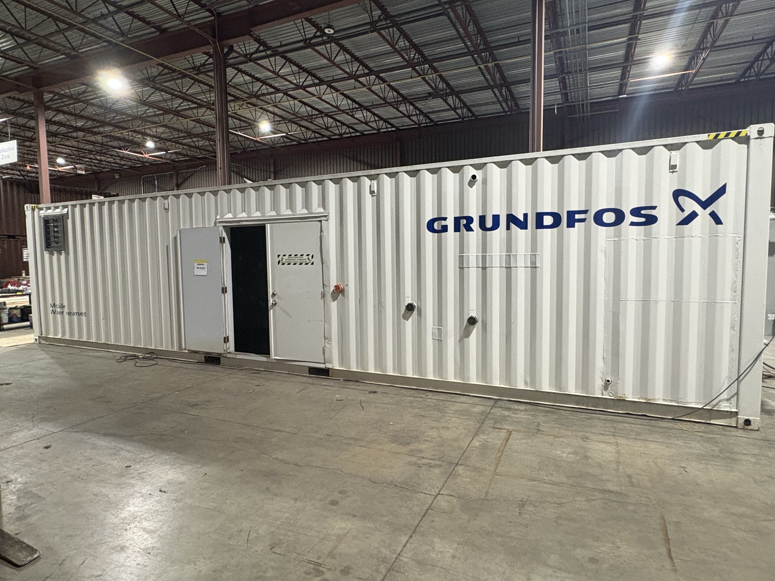 White shipping container in a large industrial warehouse with exposed steel beams and bright lights in the ceiling.